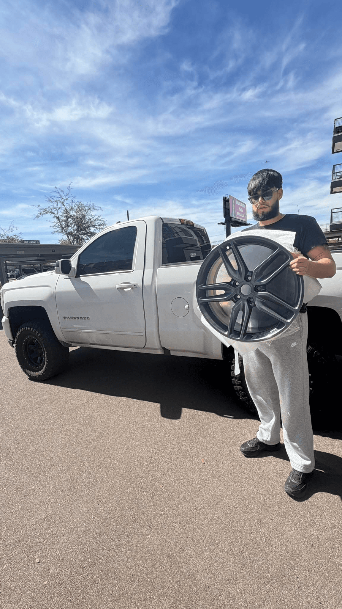 Larri customer holding a refinished dark gray wheel in front of a white pickup truck